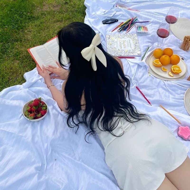 Ảnh gái xinh quay lưng đọc sách picnic trên bãi cỏ xanh