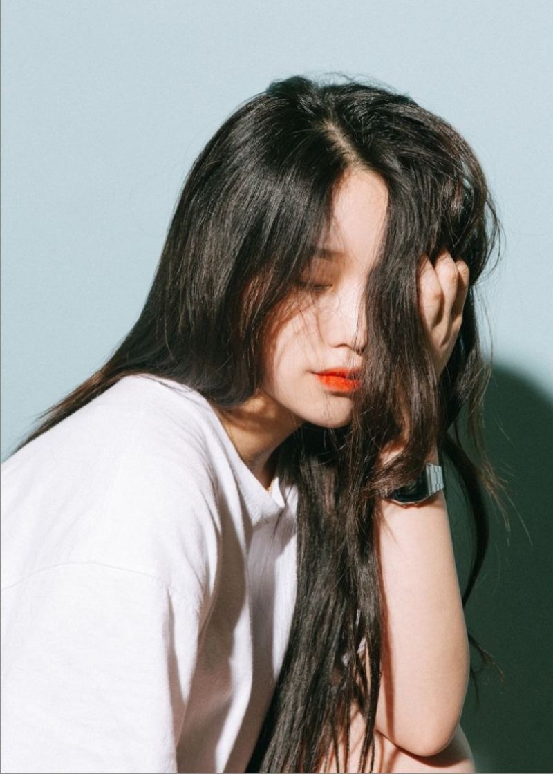 Gái xinh che mặt bằng tay trái, trước bức tường trơn