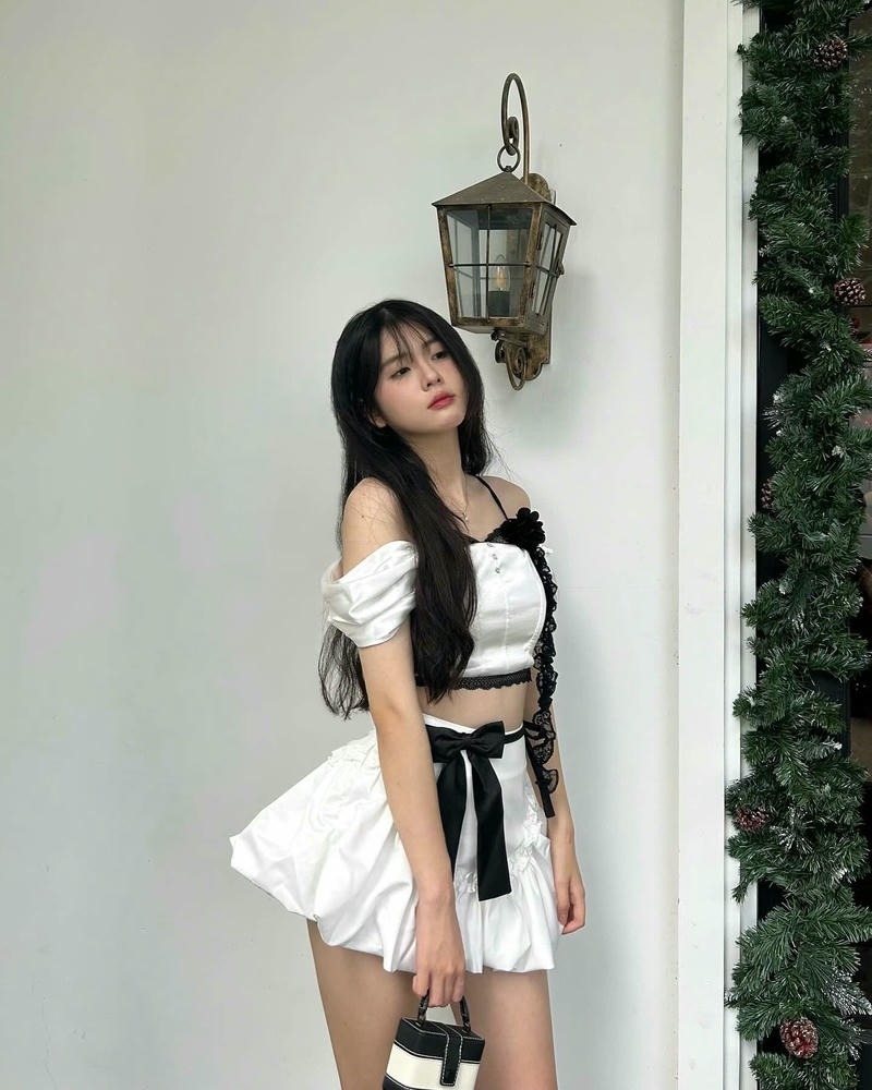 Ảnh gái xinh mặc váy ngắn màu trắng đứng bên bức tường