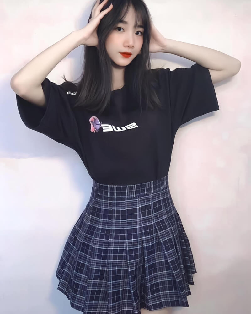 Ảnh gái xinh mặc váy ngắn xếp ly đứng trước bức tường trơn