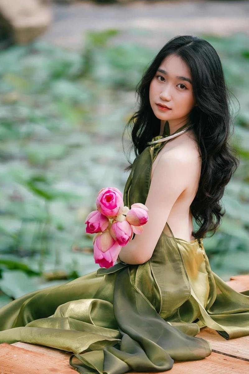 Ảnh gái xinh áo dài hở lưng ngồi nghiêng người cầm bông sen