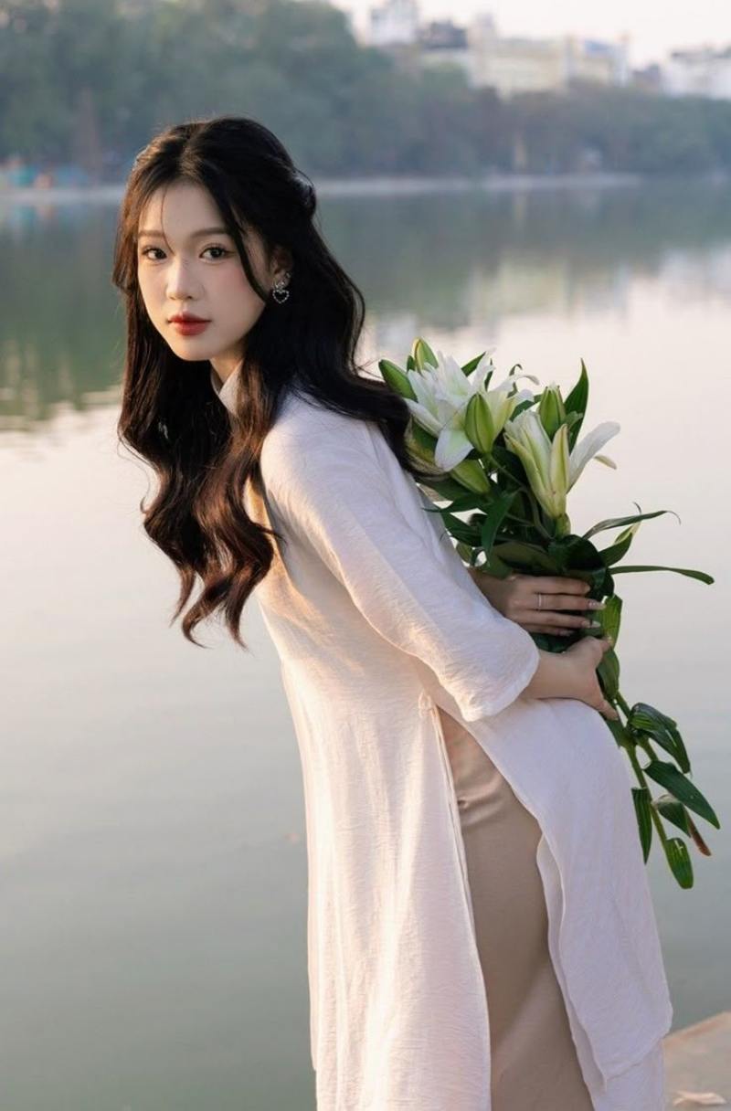 Gái xinh áo dài trắng cầm hoa ly sau lưng ở bờ hồ