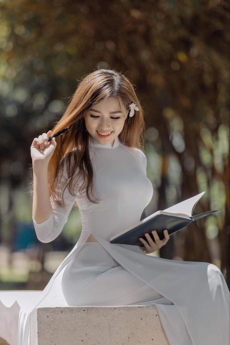 Gái xinh áo dài trắng ngồi trên ghế đá tay cầm cuốn sổ