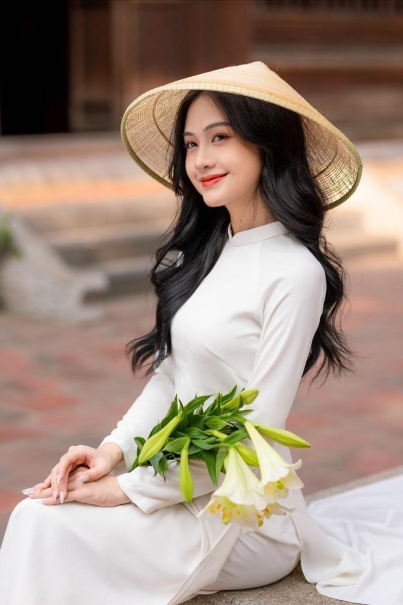 Gái xinh áo dài trắng đội nón lá, tay ôm bó hoa loa kèn
