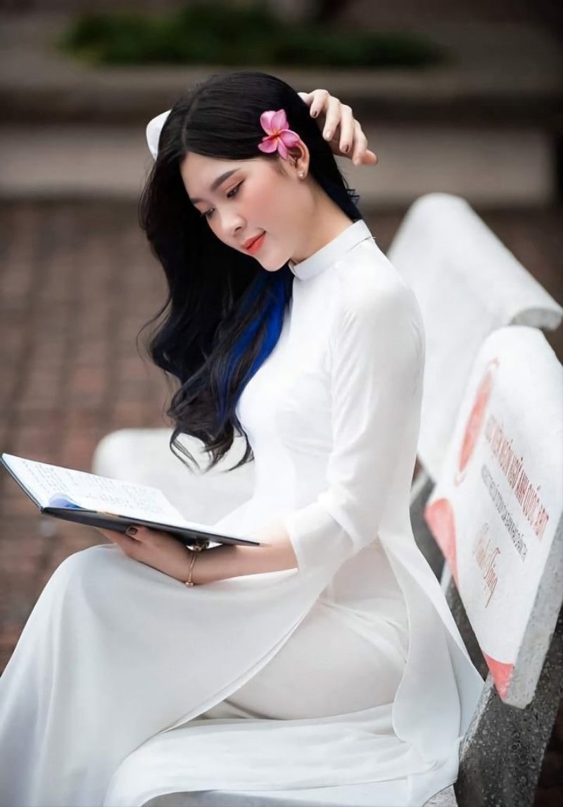 Gái xinh áo dài trắng ngồi trên ghế đá đọc cuốn sổ