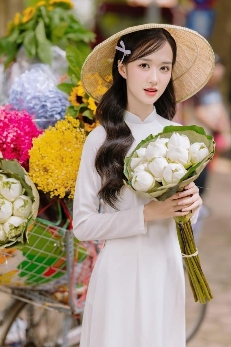 Gái xinh áo dài trắng đội nón lá cầm bông sen trắng đứng trước xe bán hoa