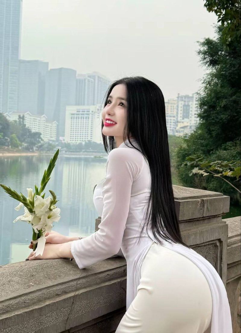 Ảnh gái xinh mông to mặc áo dài bó sát tay cầm hoa tựa vào lan can