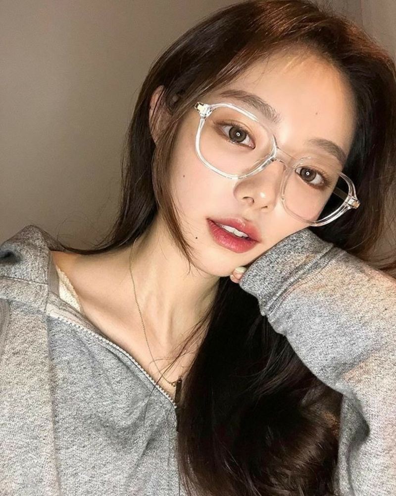 Ảnh gái xinh tóc dài đeo kính trước bức tường trơn