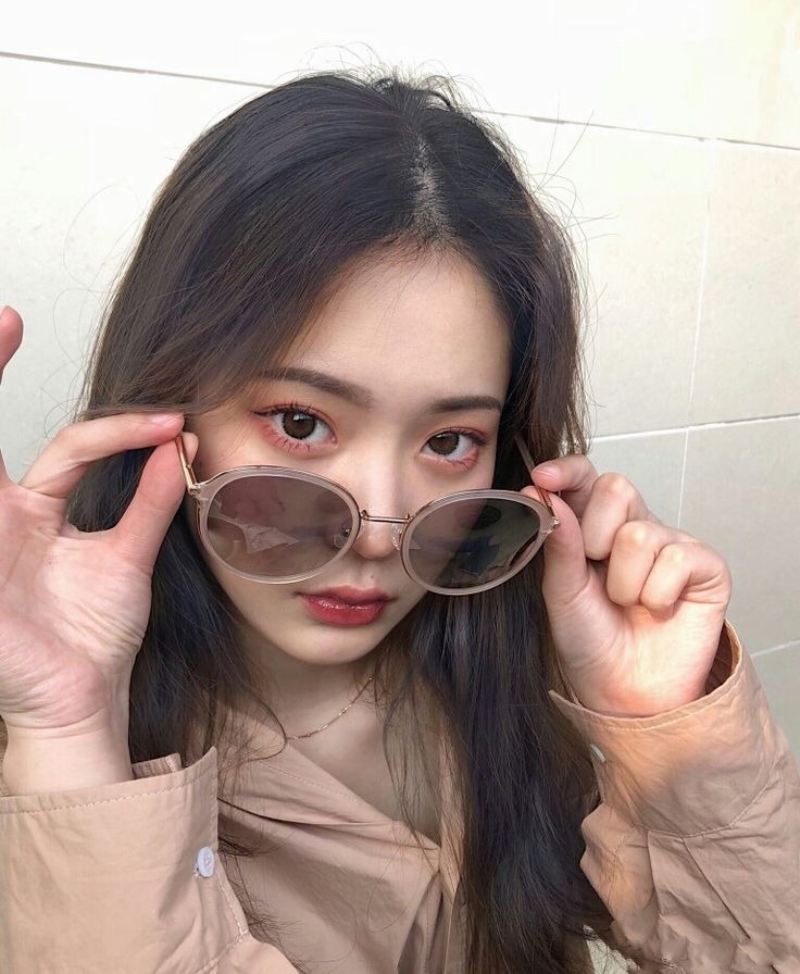 Ảnh gái xinh tóc dài đeo kính trước bức tường gạch men