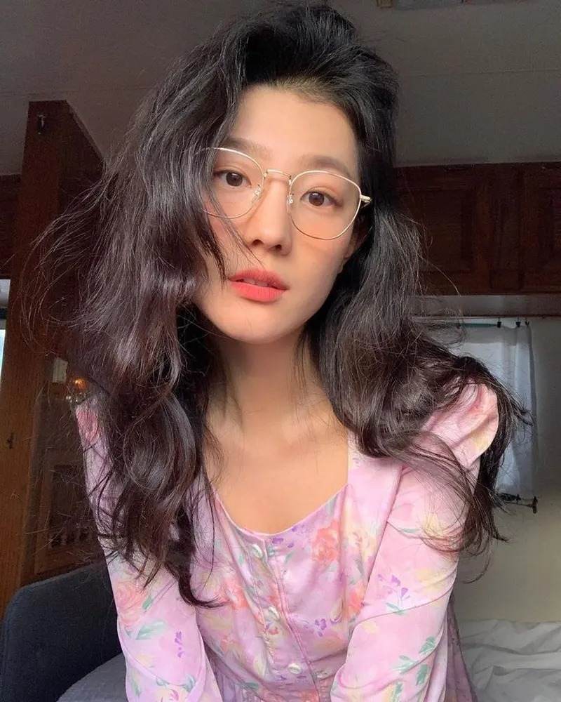 Ảnh gái xinh tóc dài đeo kính ngồi trên giường