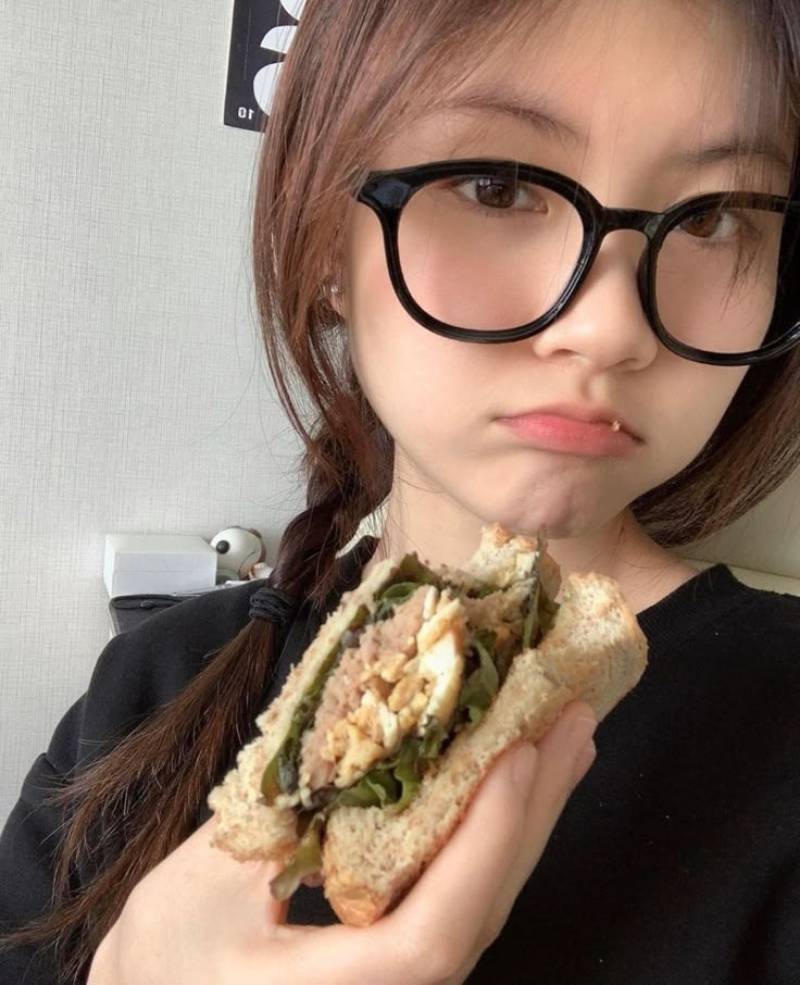 Ảnh gái xinh tóc dài đeo kính tay cầm bánh sandwich ăn