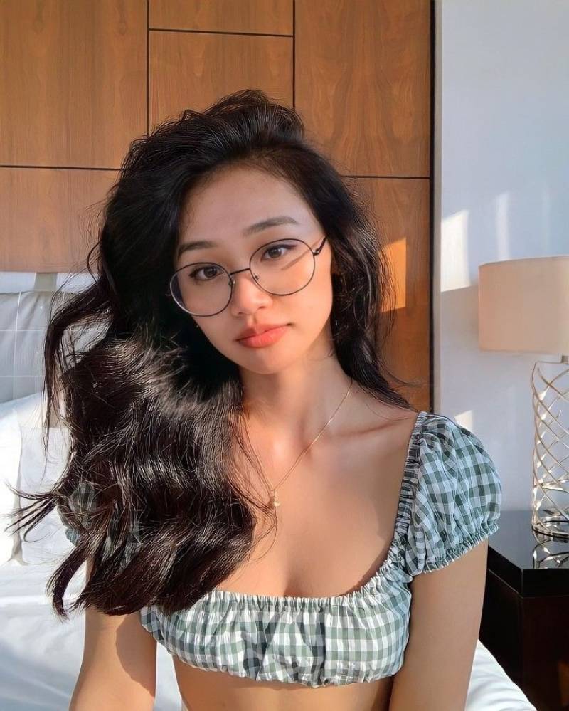 Ảnh gái xinh tóc dài đeo kính ngồi trên giường ngủ
