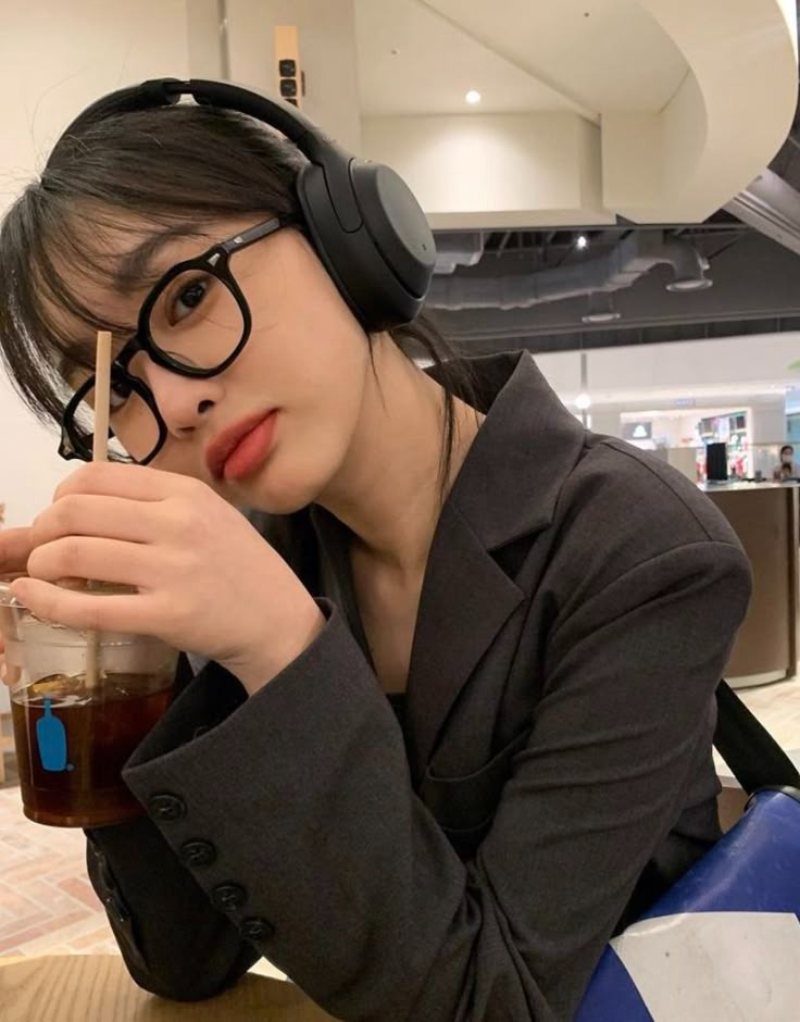 Ảnh gái xinh tóc dài đeo kính, đeo tai nghe, tay cầm ly nước ngọt