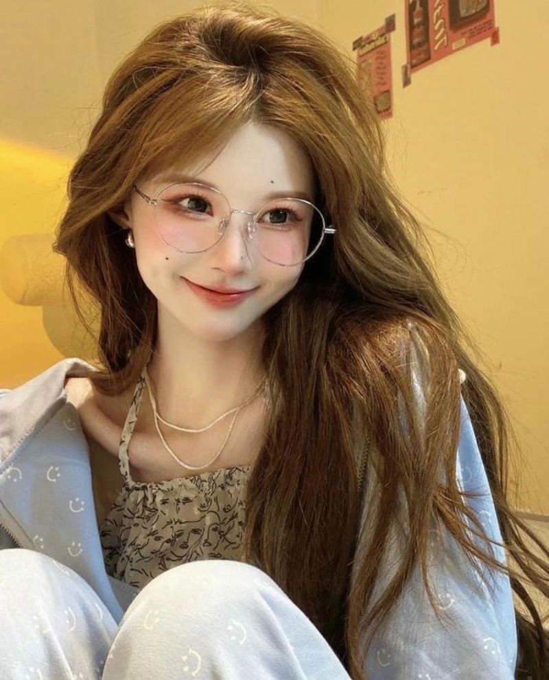 Ảnh gái xinh tóc dài đeo kính cười mĩm trước bức tường vàng