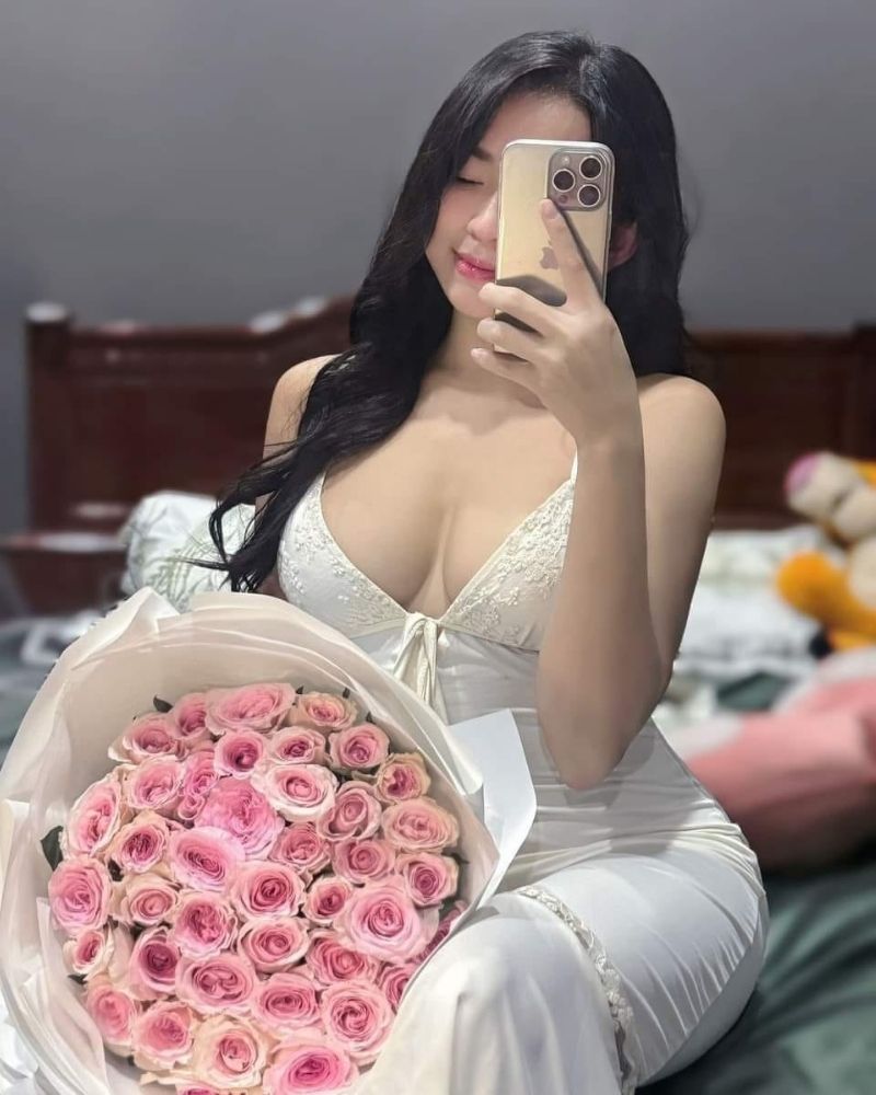 Ảnh gái xinh tự sướng bằng điện thoại, tay trái cầm bó hoa ngồi trên giường