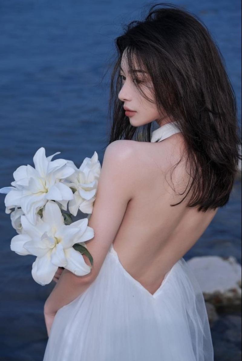 Ảnh gái xinh Trung Quốc mặc đầm trễ vai khoe lưng cầm hoa loa kèn ở biển