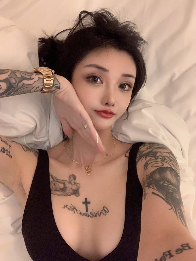 Gái xăm hình kín tay mặc áo ba lỗ đen nằm trên giường